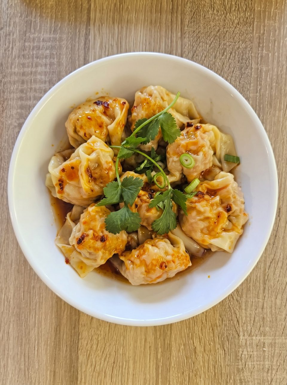 A white bowl filled with chili oil wontons, garnished with fresh cilantro and green onions.
