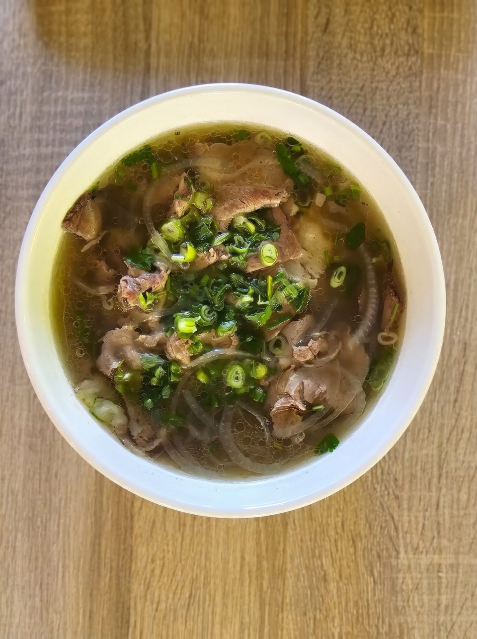 Overhead view of a white bowl filled with pho, garnished with green onions and cilantro.