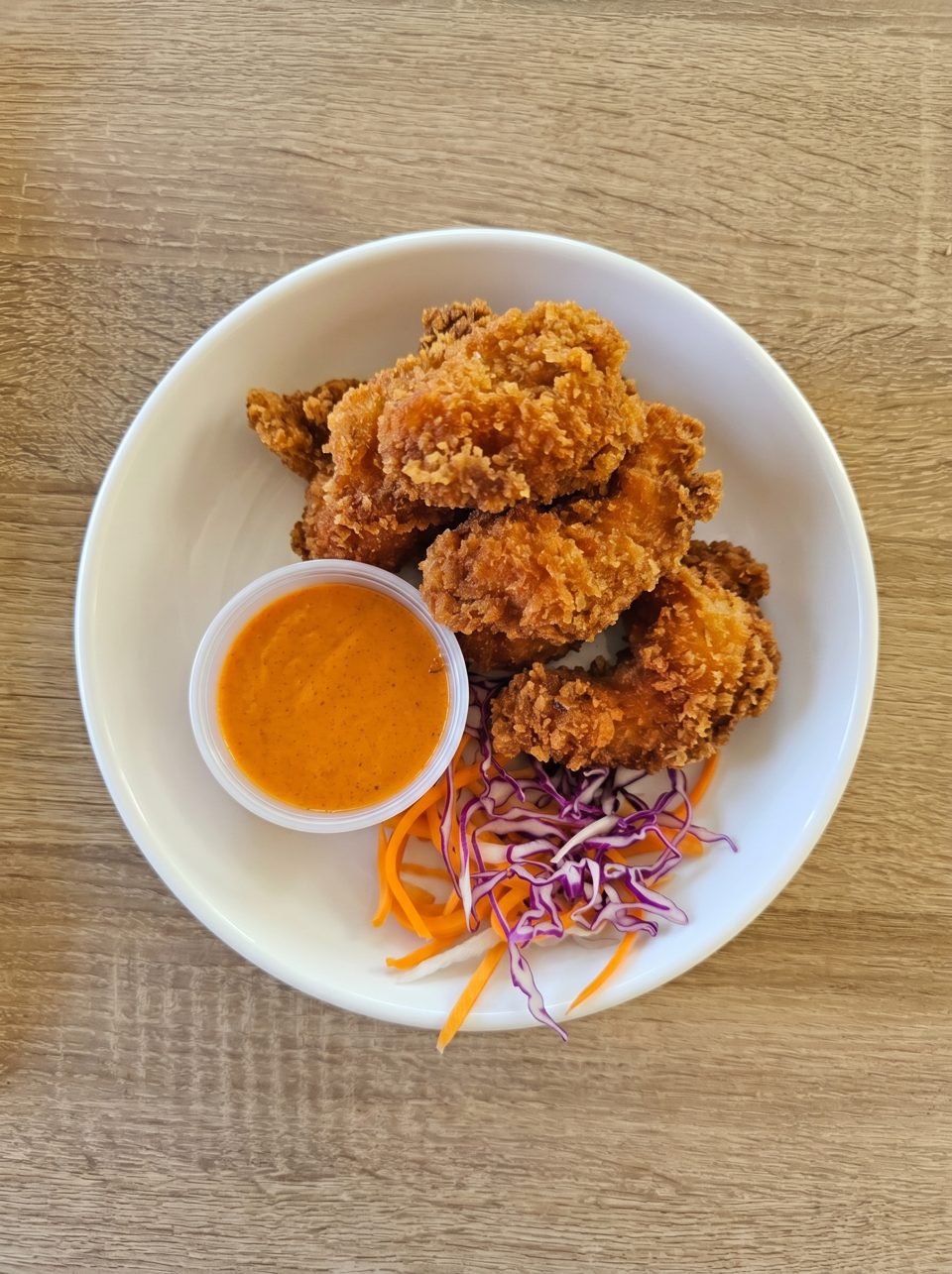 Crispy fried chicken bites with orange dipping sauce and shredded carrots and purple cabbage.